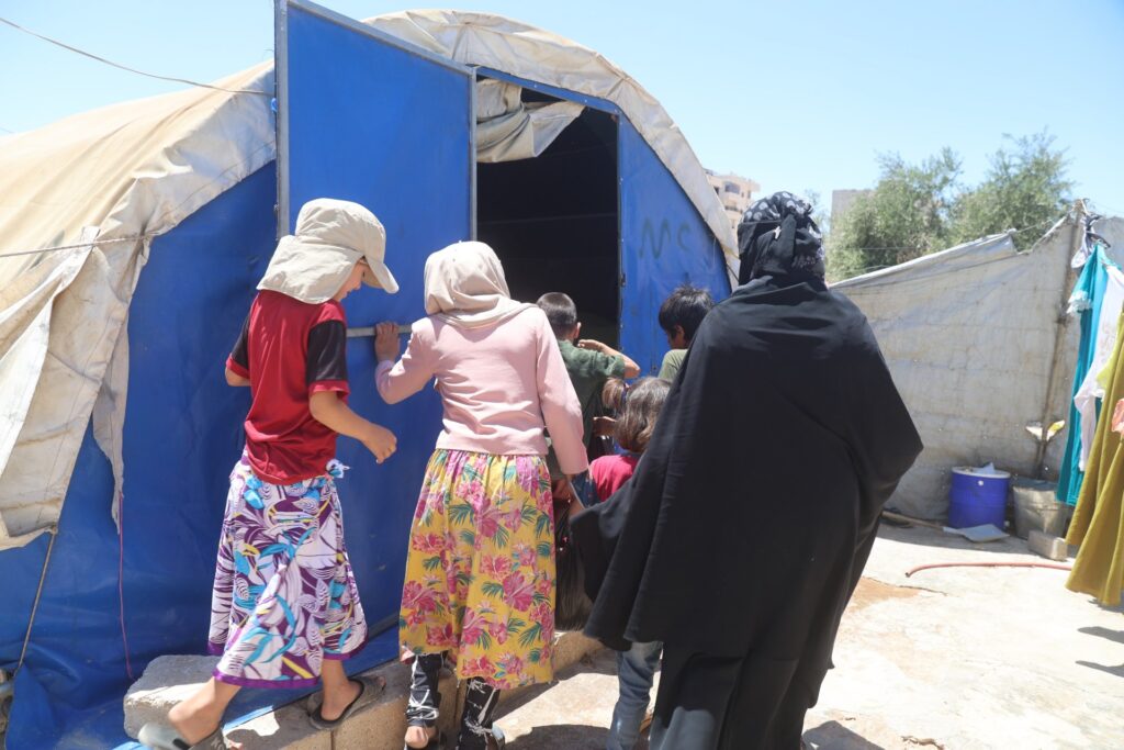 Five children and their mother walking into their temporary shelter in Northwest Syria